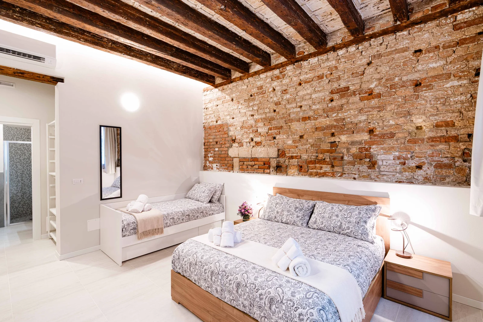 Camera dell’appartamento gestito a Campo Santa Margherita, con travi a vista e parete in mattoni
